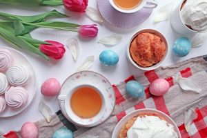 Ljus påskdukning med te, bakverk, rosa tulpaner och färgade ägg.