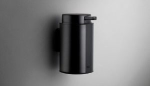 Väggmonterad svartvålpump i minimalistisk design på grå vägg.